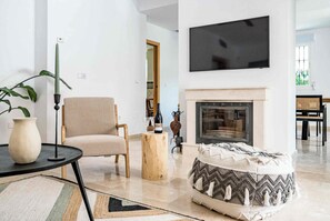 Ein Wohnzimmer mit einer Couch, einem Couchtisch, einem Kamin und einem an der Wand befestigten Fernseher.