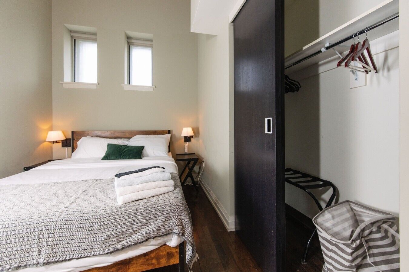 A hotel room with a bed, two bedside lamps, a window, a wardrobe, and a hanging clothes rack.