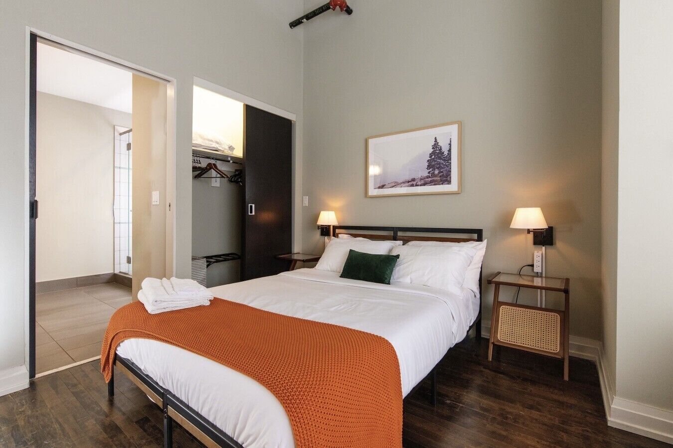 A hotel room with a bed, bedside lamps, a framed picture on the wall, and a closet with a mirror.