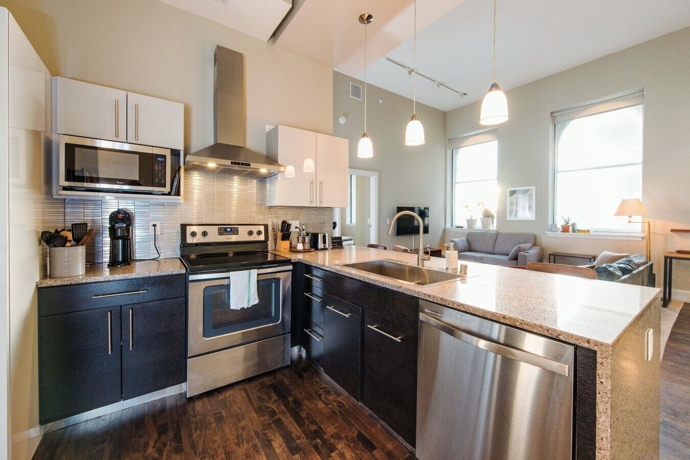 A modern kitchen with stainless steel appliances, a central island, and a dining area with a sofa.