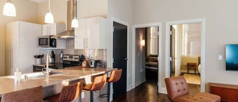 Una cocina moderna con barra, piso de madera y televisor en la sala.