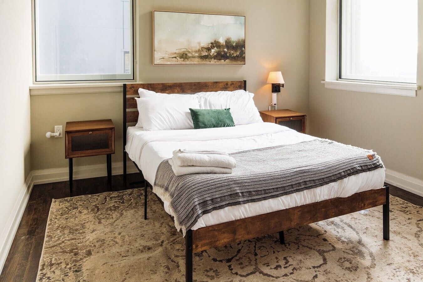 A bedroom with a bed, a nightstand, a lamp, a window, and a painting on the wall.