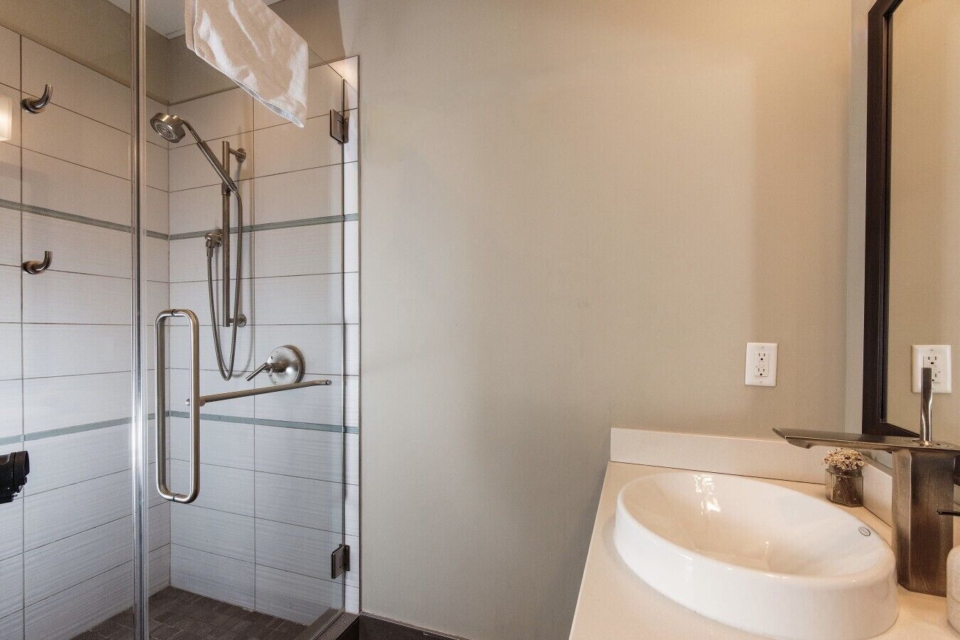 A modern bathroom with a glass shower enclosure, a white sink, and a mirror.