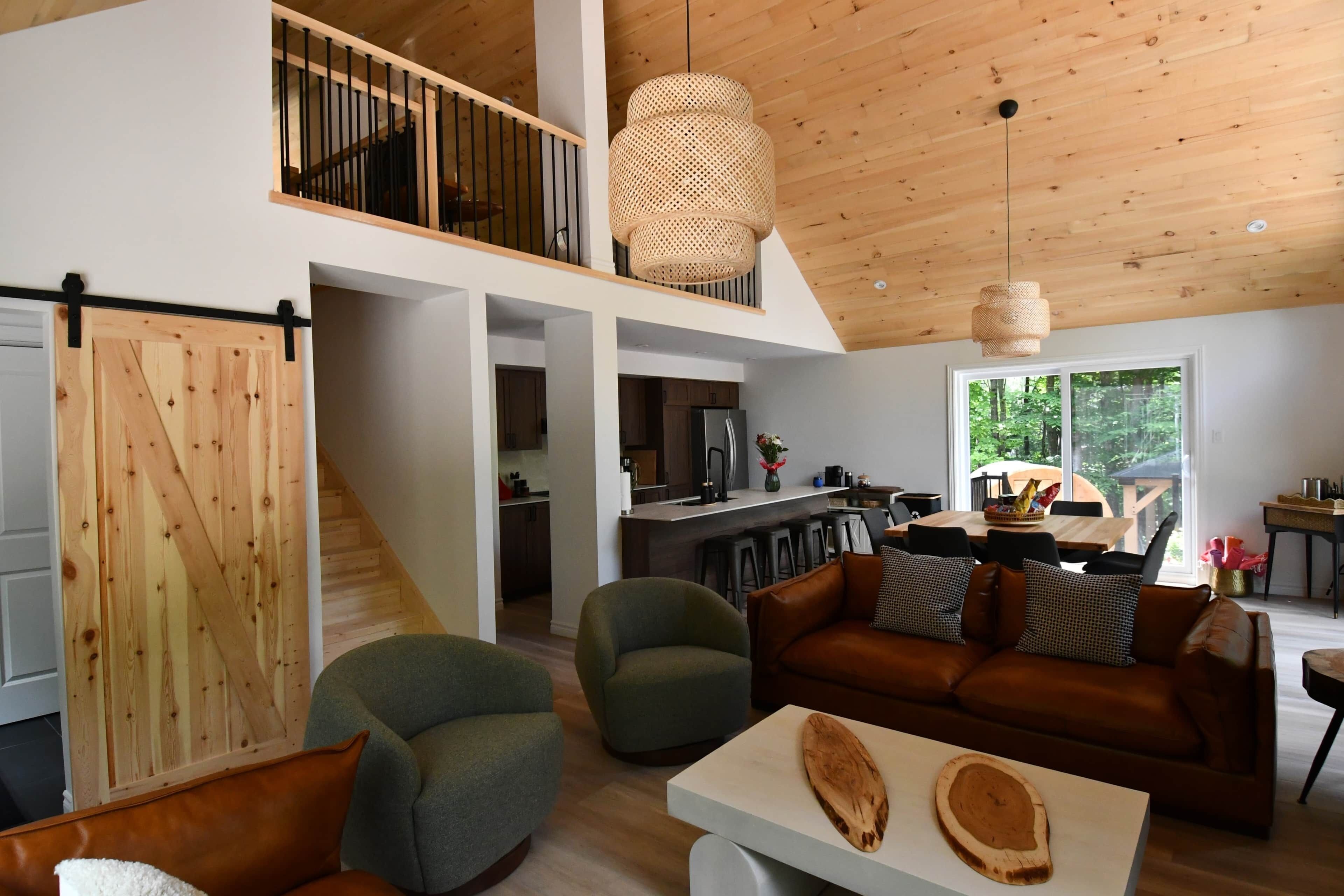 A spacious living area with a high ceiling, a dining table, and a kitchen in the background.