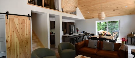 A spacious living area with a high ceiling, a dining table, and a kitchen in the background.
