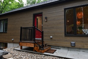 A modern building with a wooden exterior, a red door, and a black staircase leading to the entrance. - Kozy KanataTremblant (261) (Amherst)