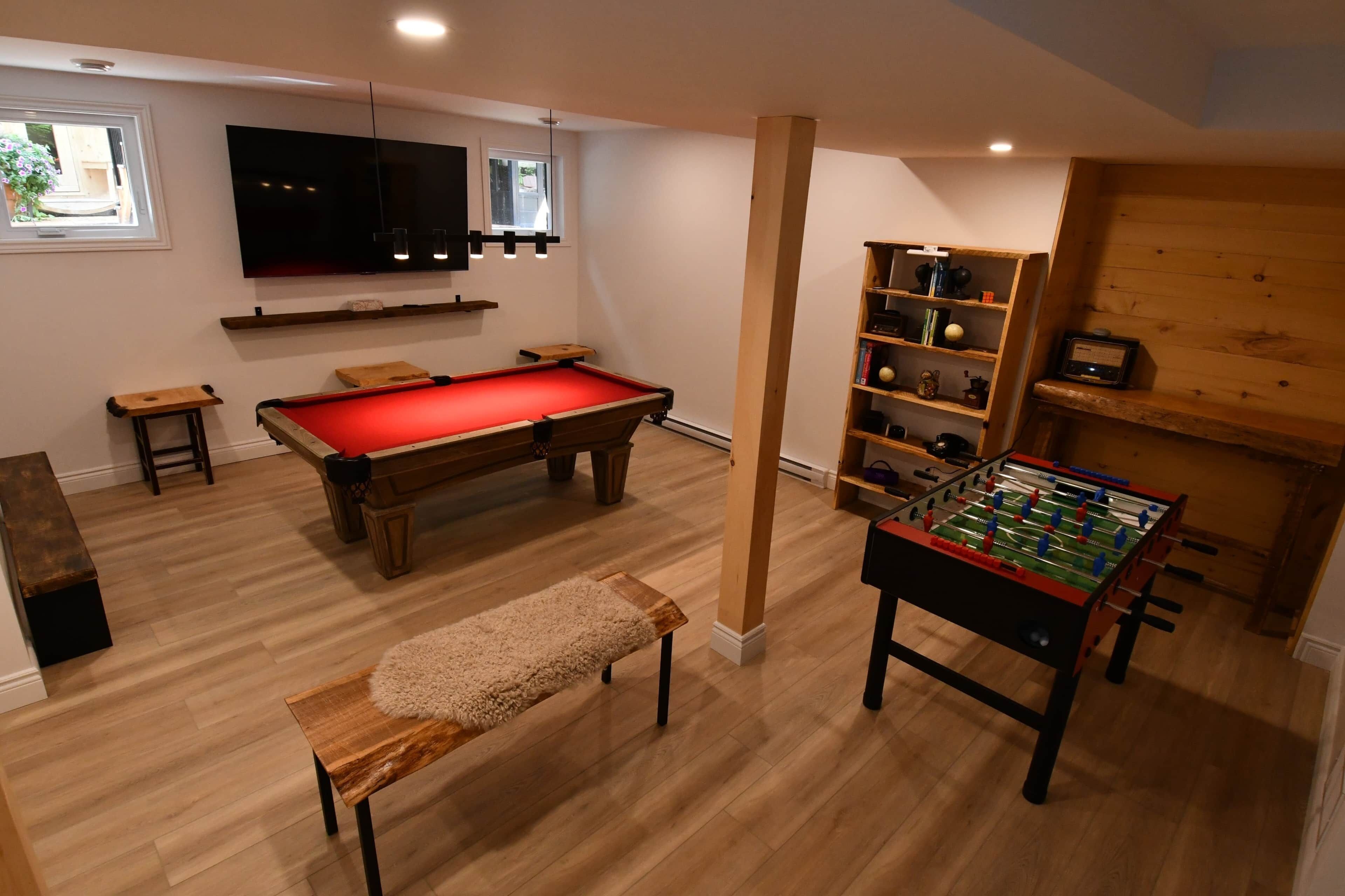 A room with a pool table, a foosball table, a bookshelf, and a television.