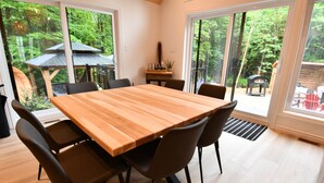 A dining area with a wooden table and chairs, large windows, and a view of a garden. - Kozy KanataTremblant (261) (Amherst)