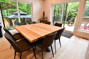 Ein Essbereich mit Holztisch und -stühlen, großen Fenstern und Blick auf einen Garten.