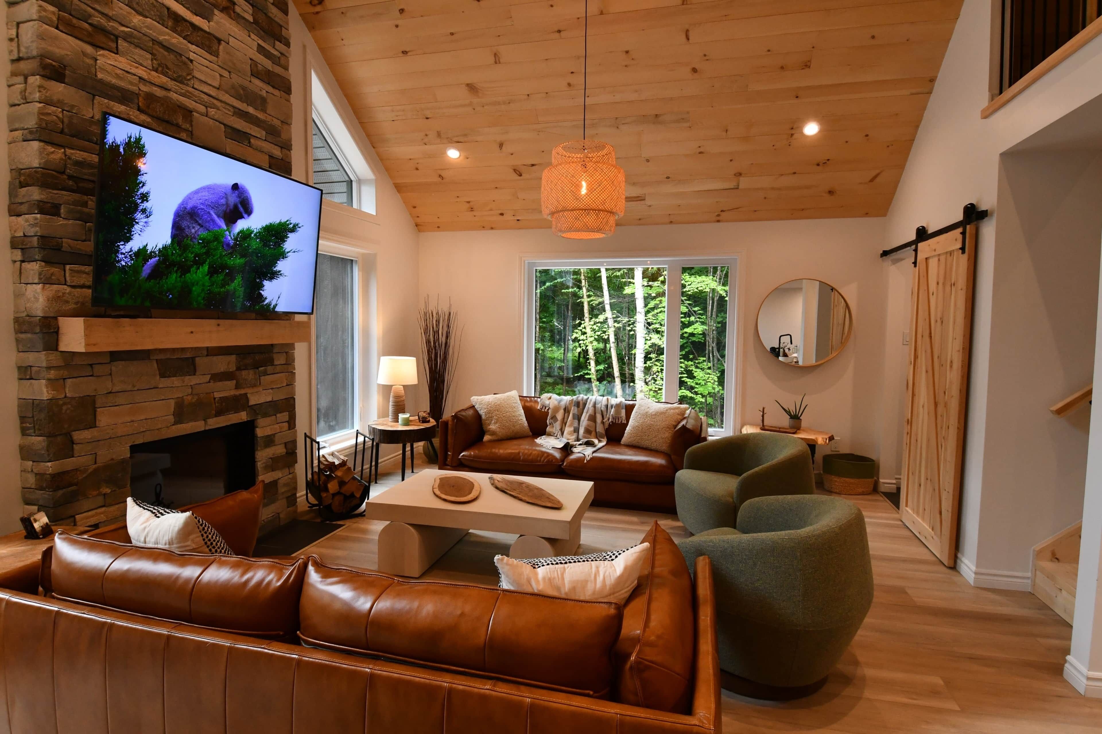 A living room with a stone fireplace, leather sofas, a coffee table, and a television mounted on the wall.