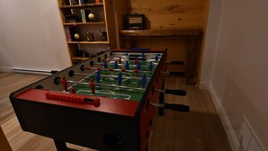 A foosball table in a room with wooden flooring and a bookshelf in the background. - Kozy KanataTremblant (261) (Amherst)
