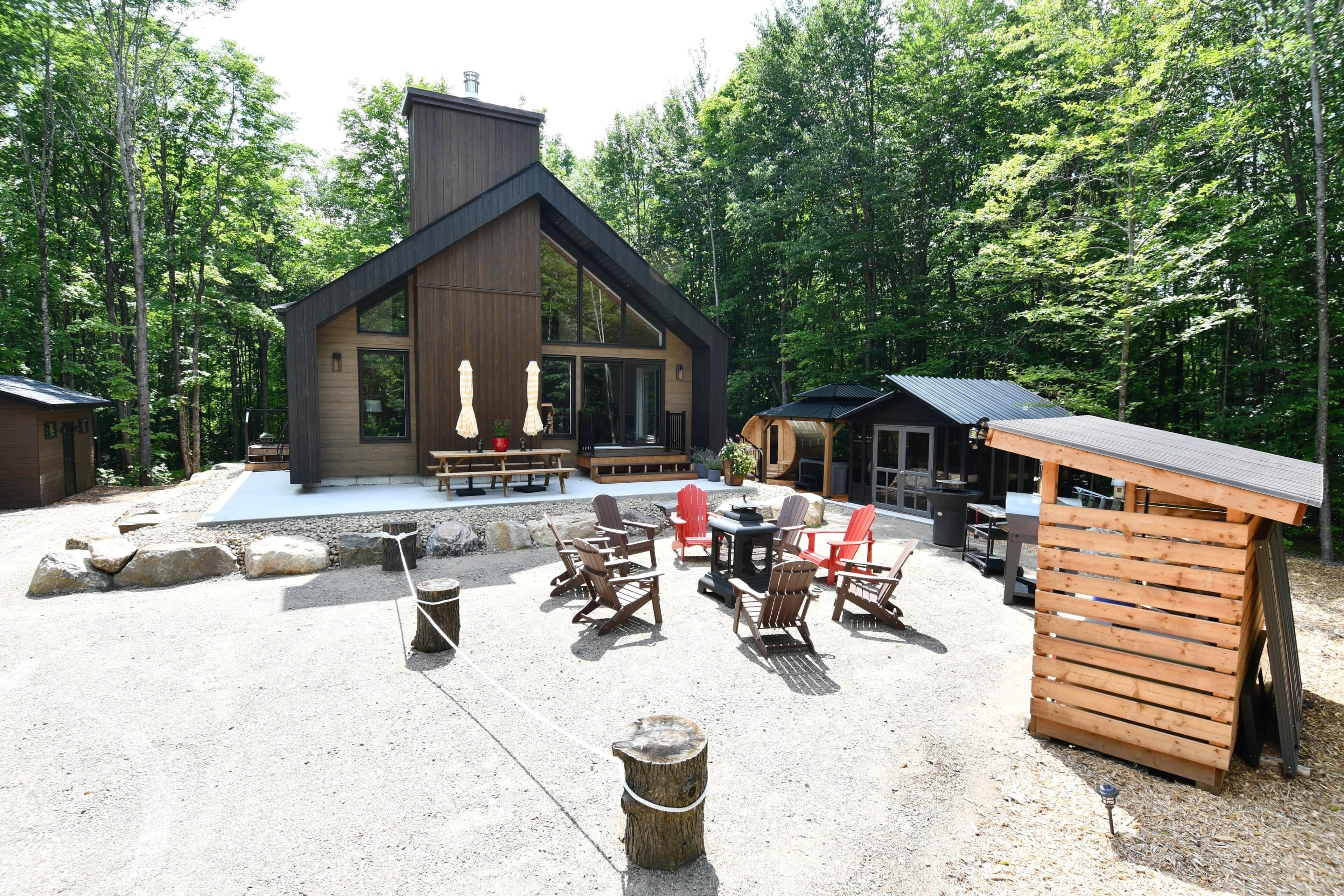 A cabin with a deck, outdoor seating, and a fire pit area surrounded by trees.