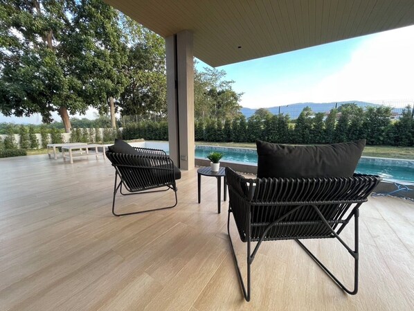An outdoor patio with two wicker chairs, a small table, and a pool in the background.