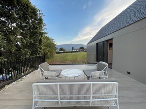 Un patio al aire libre con mesa y sillas, vista a un viñedo y un edificio moderno con techo inclinado.