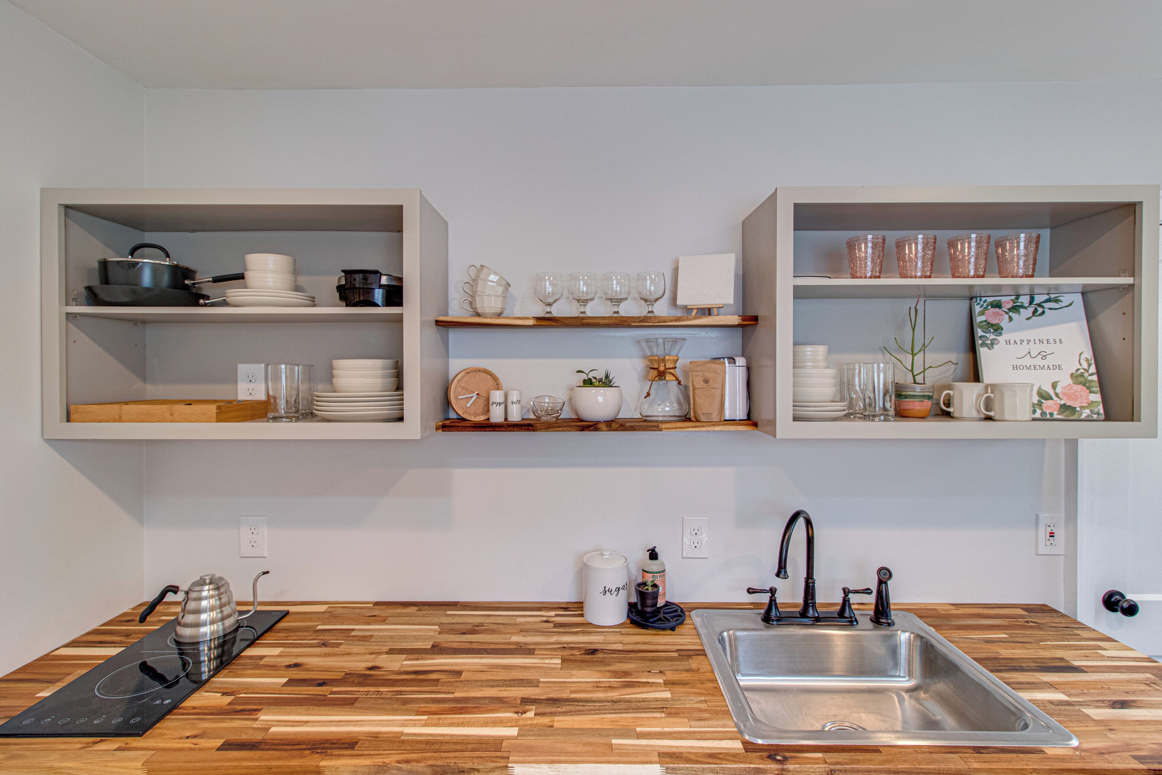 Une cuisine dotée de plans de travail en bois, d’un évier encastré et d’étagères au-dessus, où sont rangés les ustensiles de cuisine et des objets décoratifs.