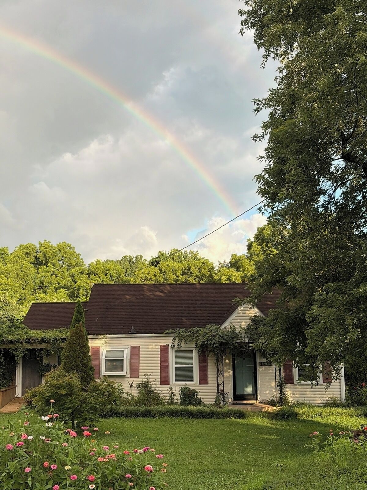 A house with a garden, a visible rainbow, and a clear sky.