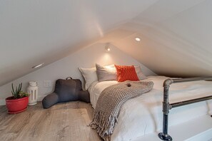 A cozy attic bedroom with a sloped ceiling, a bed with a knitted throw, and a potted plant. - Cozy Loft-Bed Bungalow near DWTN Nashville (Nashville)