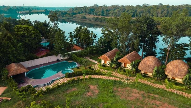 A resort with a swimming pool, thatched-roof huts, and a view of a lake.