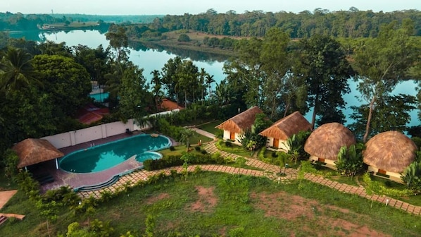 A resort with a swimming pool, thatched-roof huts, and a view of a lake.