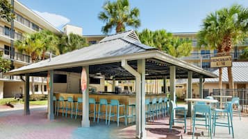 A covered outdoor bar area with multiple seating arrangements, including bar stools and tables.