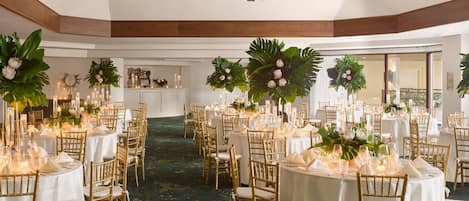 Une salle de banquet avec des tables rondes, des chaises dorées et des centres de table floraux.
