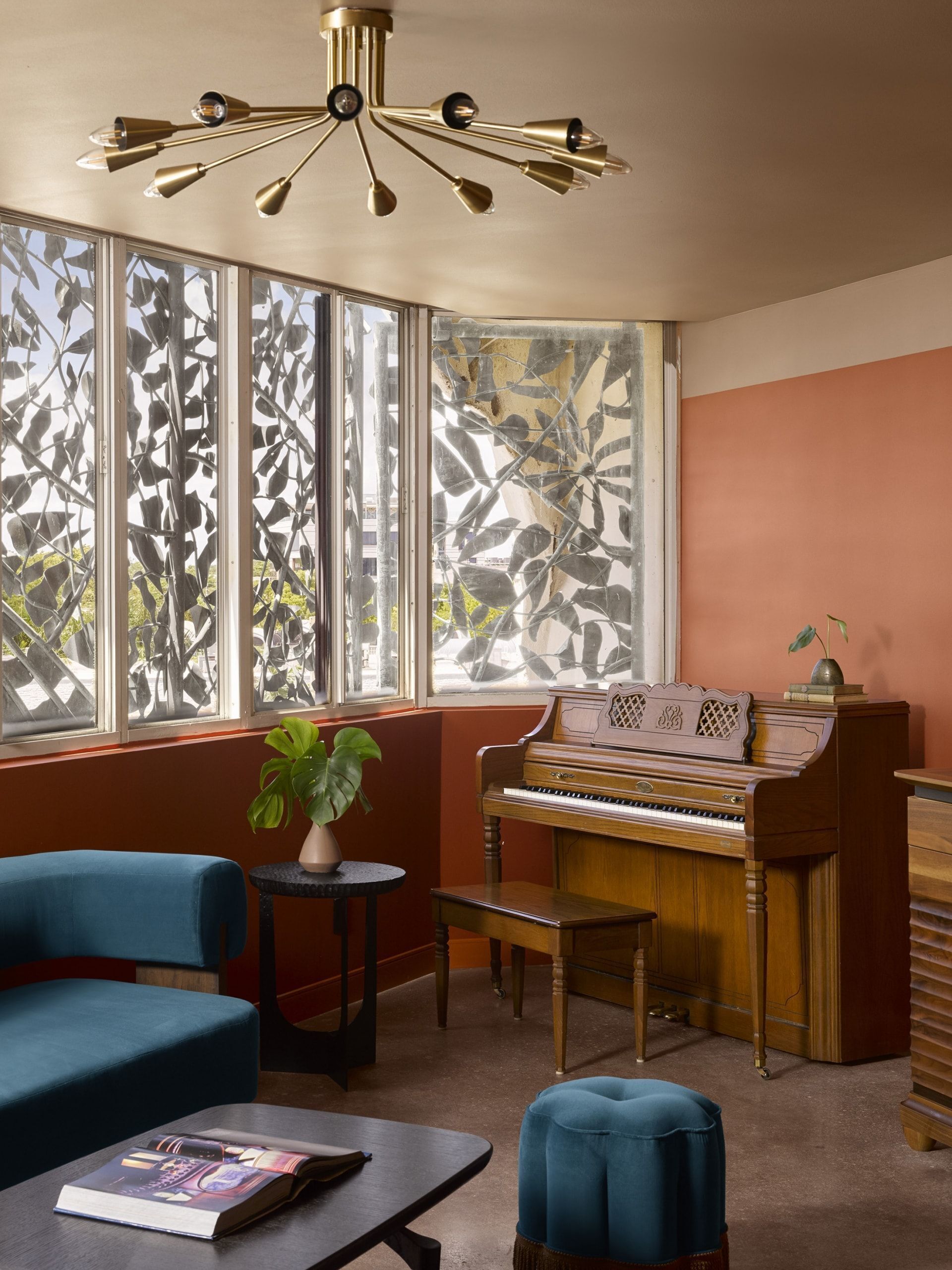 Una habitación con un piano, un sillón azul, una mesita con un libro y una planta.