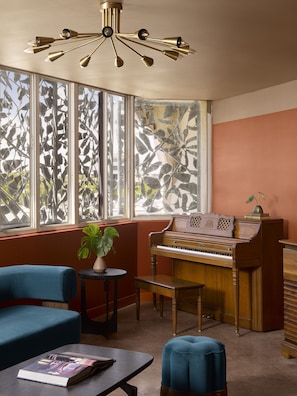 Una habitación con un piano, un sillón azul, una mesita con un libro y una planta.
