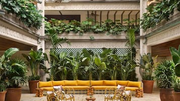 A multi-level atrium with a central yellow sofa, wicker chairs, and potted plants.