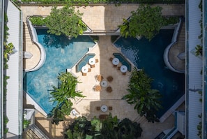 Un espace piscine aménagé sur le toit, comprenant deux piscines, entouré de chaises longues et de tables, et ombragé par de grands arbres.