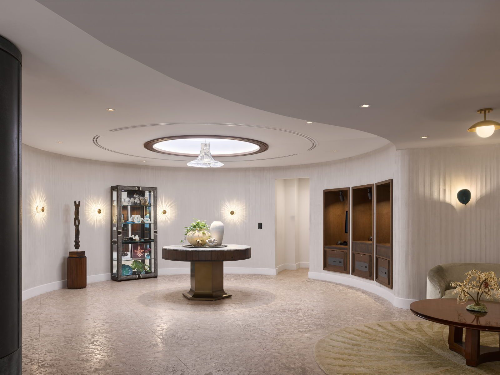 A spacious lobby with a central round table, a glass cabinet with decorative items, and a seating area with a round table.