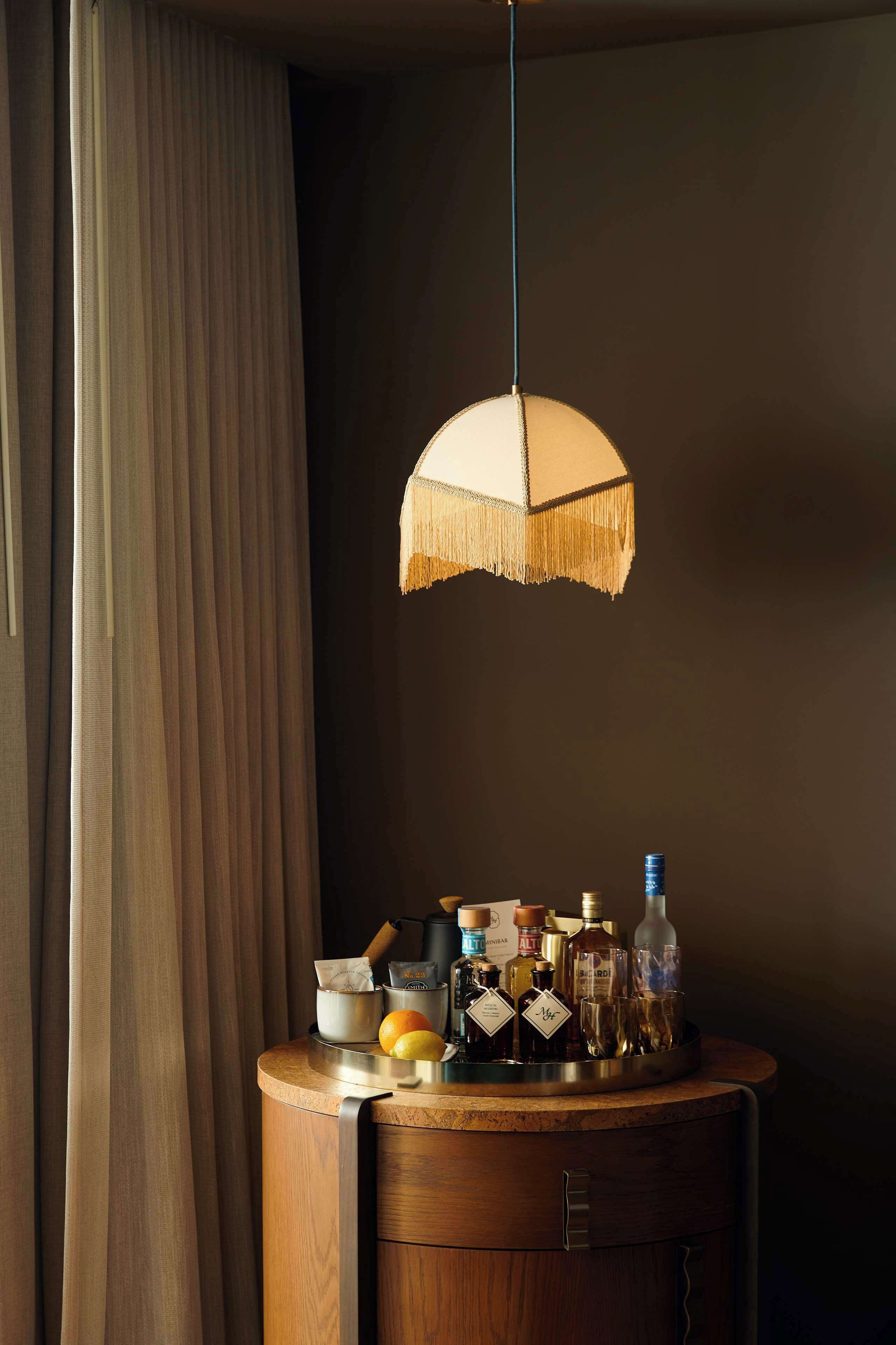 Una habitación con un armario de madera, una lámpara colgante y varios botellas y vasos sobre el armario.