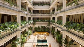 Un atrio de varios niveles con abundante vegetación, una zona de estar central y detalles arquitectónicos ornamentales.