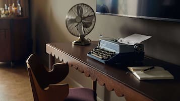 A wooden desk with a typewriter, a fan, and a chair.