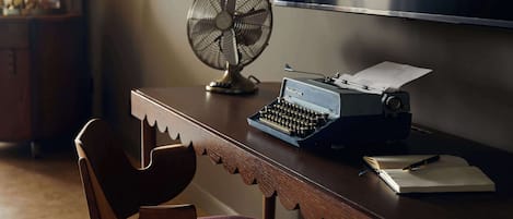 Un escritorio de madera con una máquina de escribir, un ventilador y una silla.