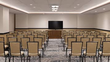 A conference room with rows of chairs, a large flat-screen TV, and a patterned carpet.