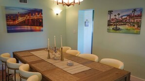 A dining room with a wooden table, white chairs, and three paintings on the walls. - Large Waterfront Retreat with Deep Water Dock! (St Augustine)