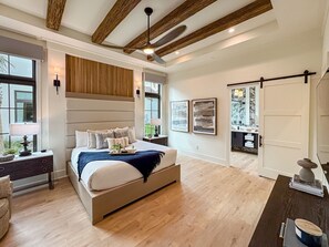 A spacious bedroom with a large bed, wooden ceiling beams, a ceiling fan, and a view of the outdoors through a window. - Luxury Home w/ Pool, Hot Tub | Gated Resort (Kissimmee)