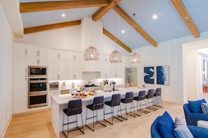 A modern kitchen with white cabinetry, stainless steel appliances, and a central island with bar stools. - Luxury Home w/ Pool, Hot Tub | Gated Resort (Kissimmee)