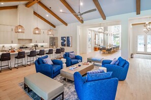 A spacious living area with blue sofas, a coffee table, and a kitchen in the background.