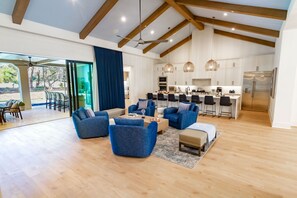 Amplia sala de estar con muebles modernos, una cocina con armarios blancos y un ventanal con vistas a un jardín.