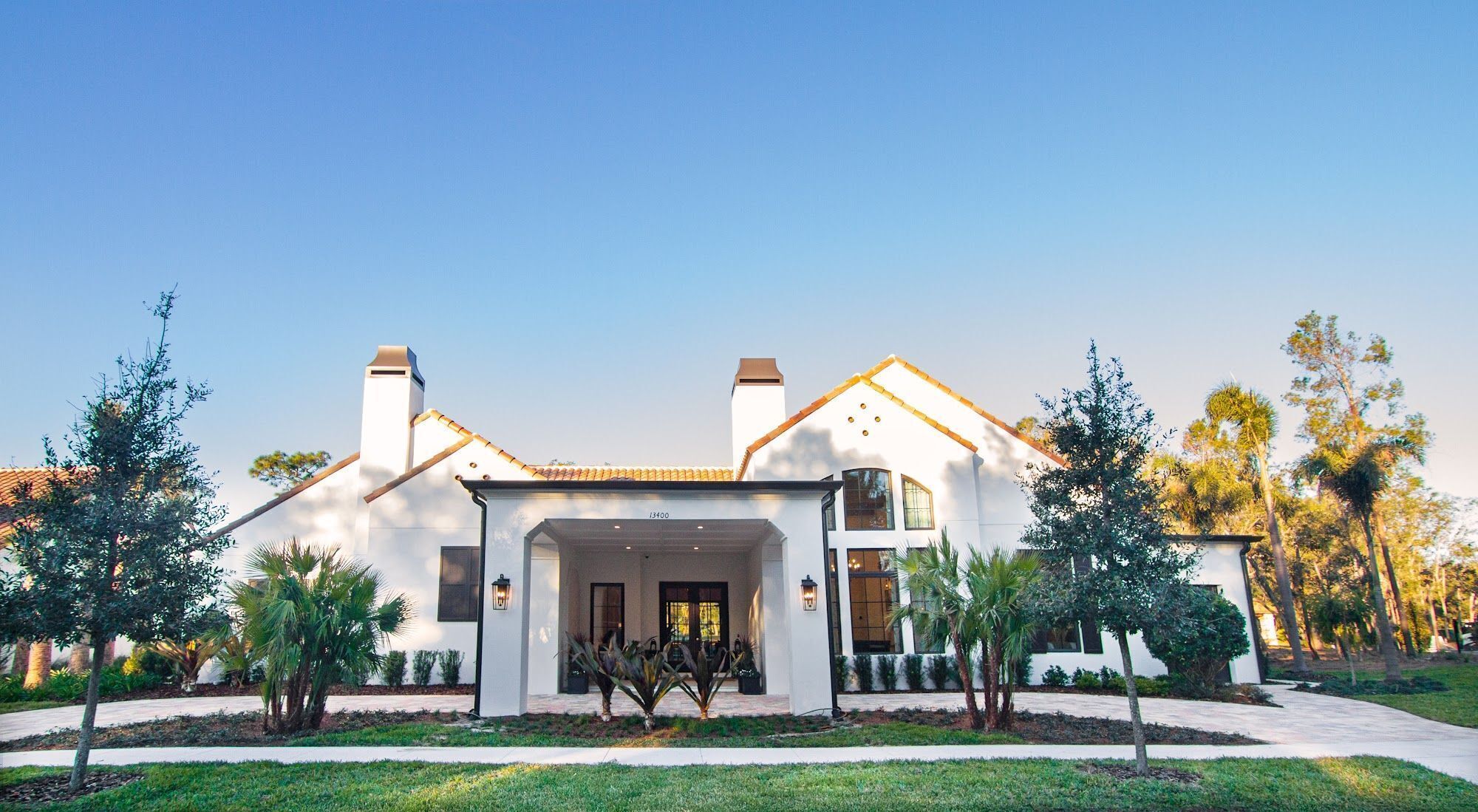 A two-story house with a white exterior, a covered entrance, and a well-maintained front yard with palm trees.