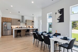 Ett modernt kök med en central köksö, barstolar och en matplats med plats för sex personer.