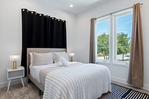 A bedroom with a bed, two bedside tables, a window with curtains, and a view of trees. - Dallas Retreat, Mins to DT, Hot Tub & Big Backyard (Dallas)