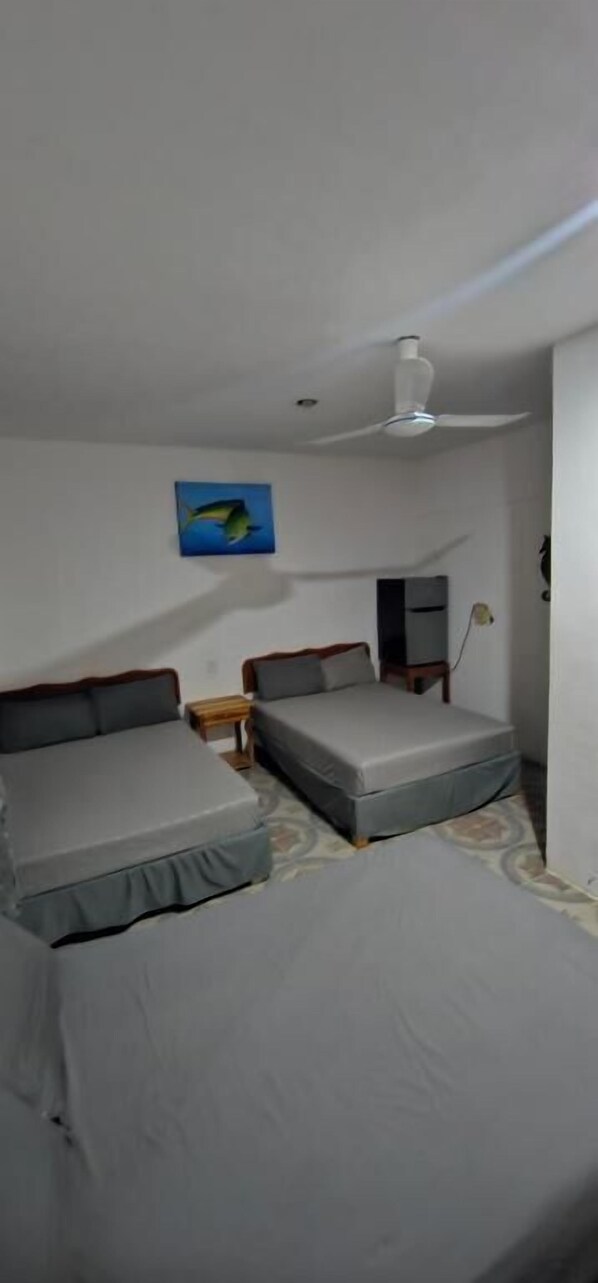 A room with two beds, a ceiling fan, a nightstand, and a wall-mounted TV.