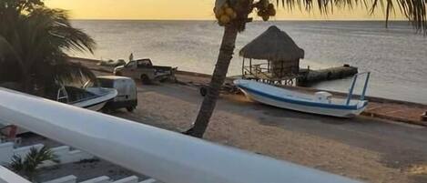 A beach view with a palm tree, a thatched hut, and a boat.