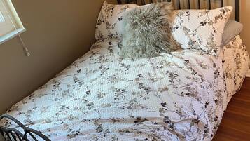 Una cama individual con una colcha estampada de flores, un cojín redondo y un cabecero.