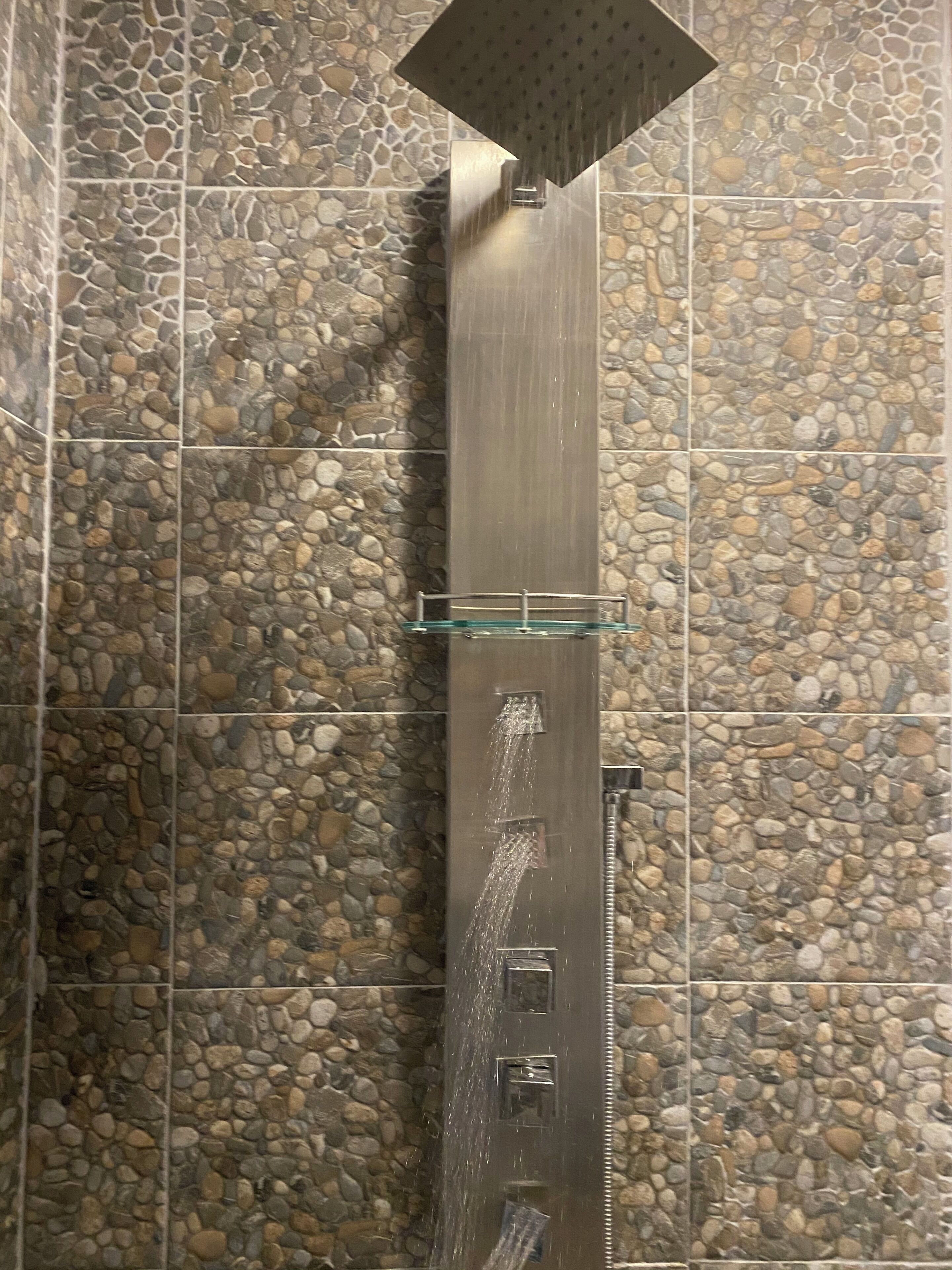 A shower with multiple nozzles against a wall with a pebble pattern.