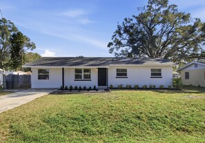 A single-story house with a front porch, a small front yard, and a tree to the right.