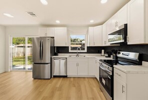 A modern kitchen with stainless steel appliances, white cabinetry, and a large window. - Modern 4BR Retreat | Near Lakeland and Legoland (Auburndale)