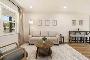 A living room with a sofa, a round wooden coffee table, a floor lamp, and a dining table with benches. - Modern 4BR Retreat | Near Lakeland and Legoland (Auburndale)